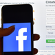 A person holds an iPhone displaying the Facebook app logo in front of a computer screen showing the facebook login page on August 3, 2016 in London, England.